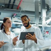 Two epidemiologists in a laboratory look at a tablet.