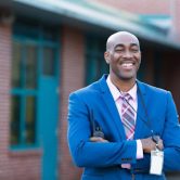A smiling education administrator stands in front of a school building.