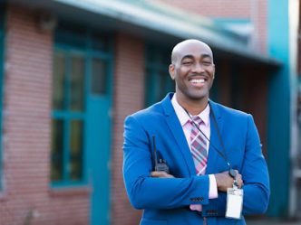 A smiling education administrator stands in front of a school building.