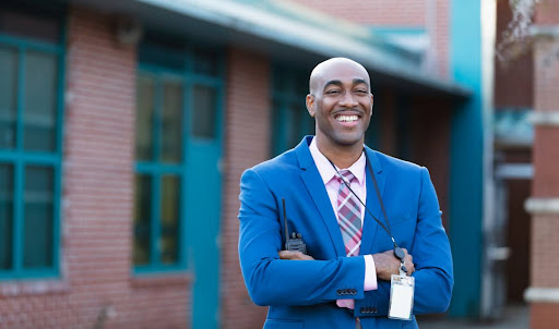 A smiling education administrator stands in front of a school building.