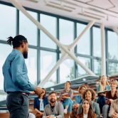 A training and development manager speaks to a group of professionals in a conference hall.