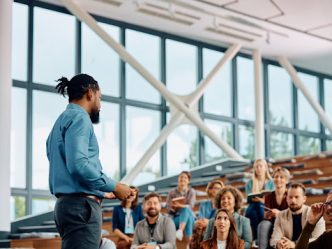 A training and development manager speaks to a group of professionals in a conference hall.