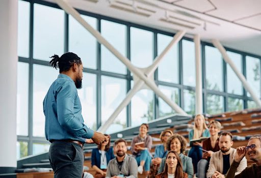 A training and development manager speaks to a group of professionals in a conference hall.
