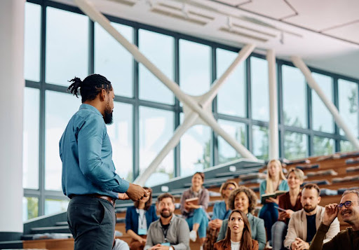 A training and development manager speaks to a group of professionals in a conference hall.