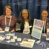 Representatives from the DCG smile while sitting at a recruiting table.