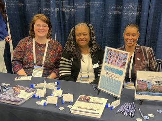 Representatives from the DCG smile while sitting at a recruiting table.