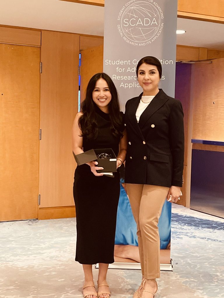 student smiles with award, standing by her mentor