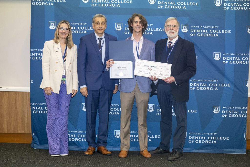 Winner holds award next to presenters.