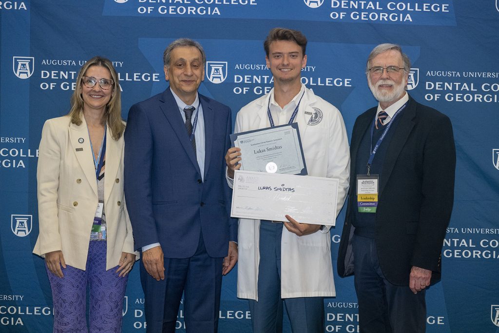 Winner holds award next to presenters.