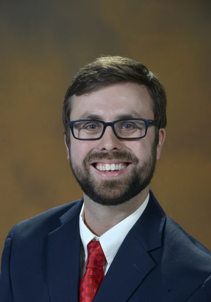 A bearded man wearing glasses smiles at the camera.