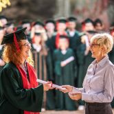 A college dean hands a graduate a diploma during a graduation ceremony.