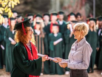 A college dean hands a graduate a diploma during a graduation ceremony.