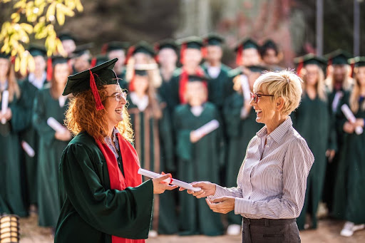 A college dean hands a graduate a diploma during a graduation ceremony.